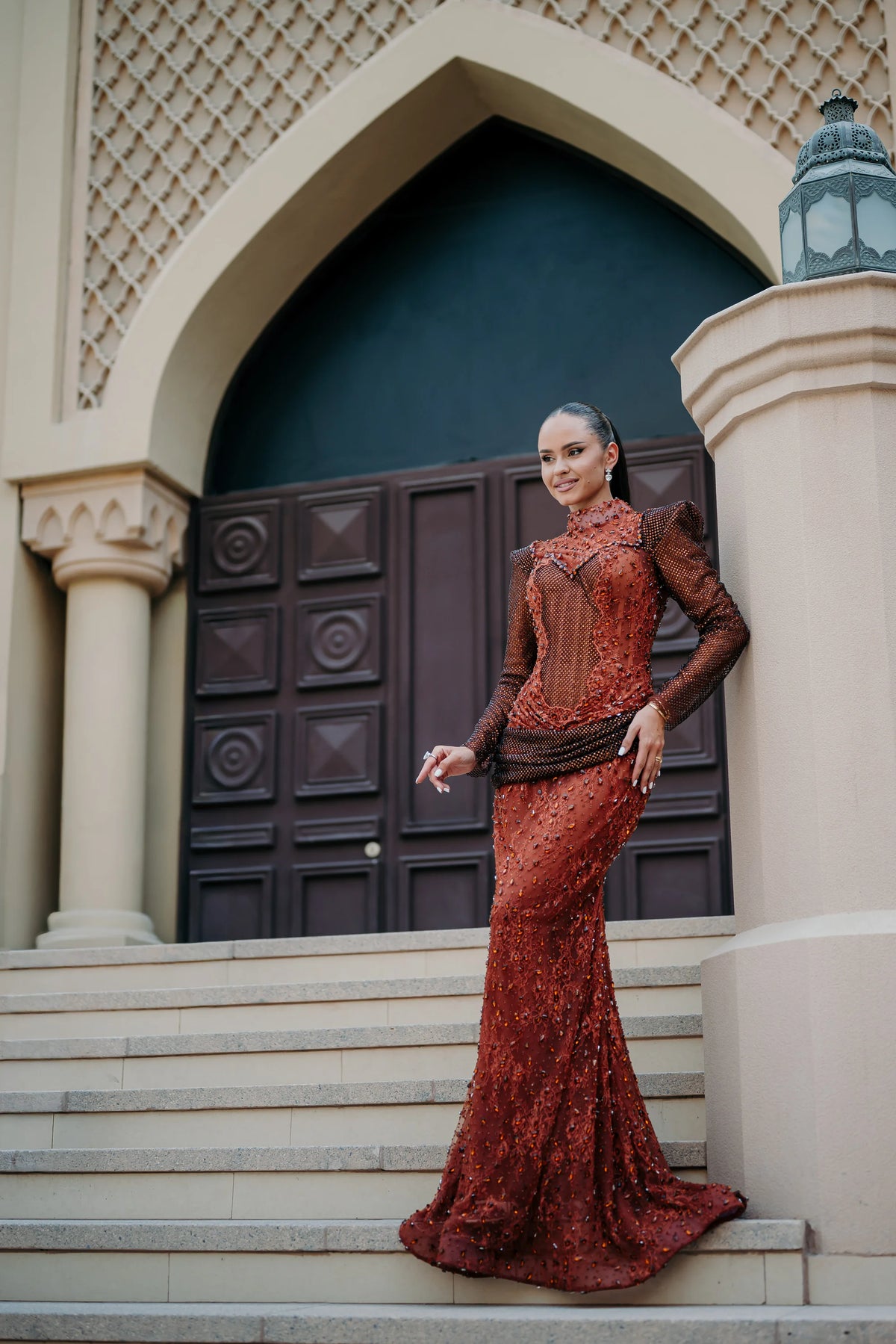 Sihëna Carnelian Sarabande — rust high-neck long-sleeve mermaid gown with beaded sheer sleeves and a beaded lace skirt.