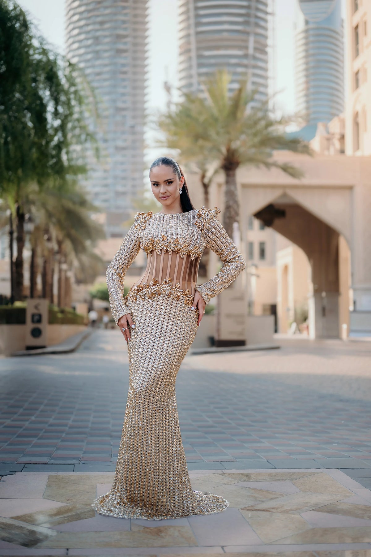 Sihëna Heliodor Colonnade — gold high-neck long-sleeve column gown with vertical gold beading and a sheer corset midriff.