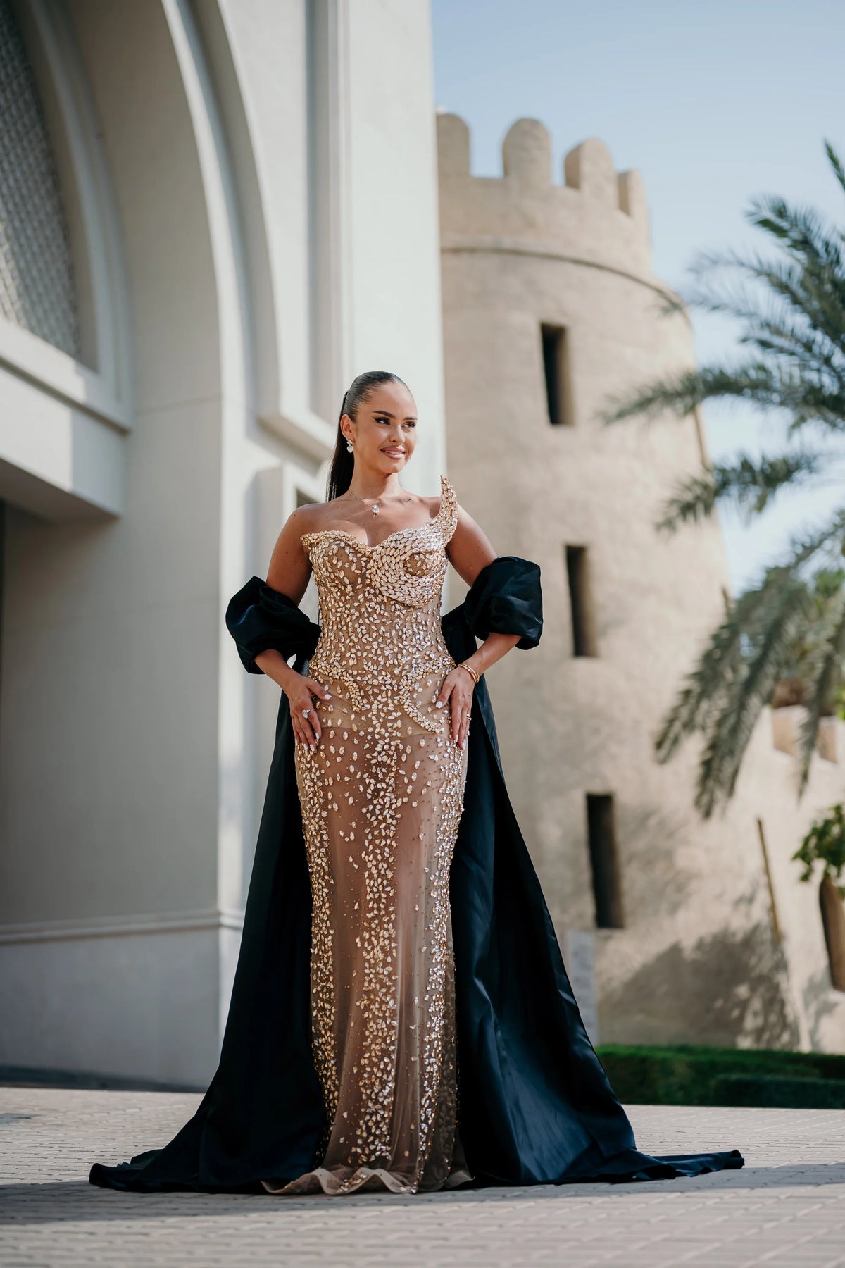 Sihëna Nacre Penumbra — champagne strapless sleeveless column gown with a crystal bodice and a separate black satin cape.