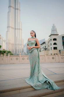 Sihëna Seaglass Idyll — sage-green square-neck spaghetti-strap column gown with pearl floral beading and a satin cape.